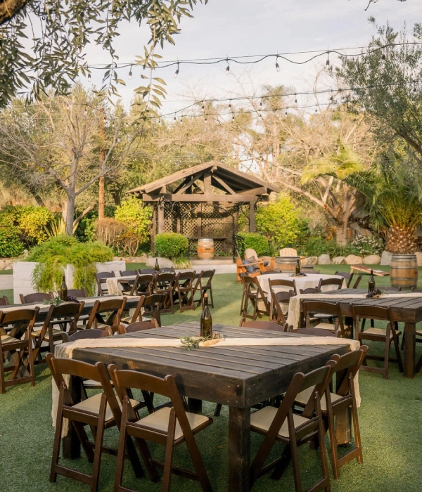 Outdoor garden event setup with wooden tables and chairs under string lights.